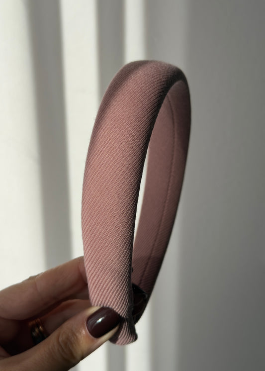 Pink headband held by a hand against a white background