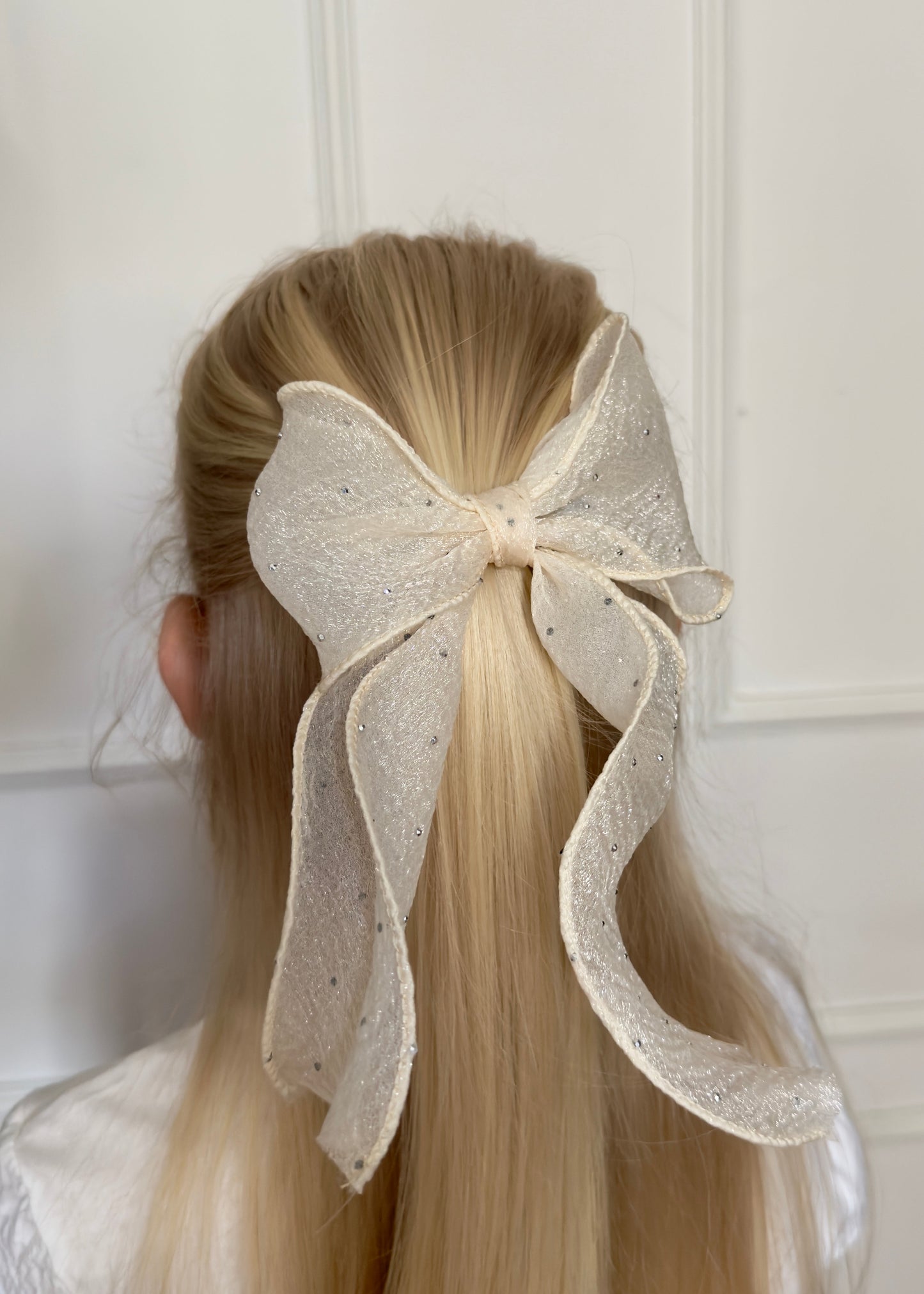 Person with long blonde hair wearing a large decorative bow in the hair against a white background