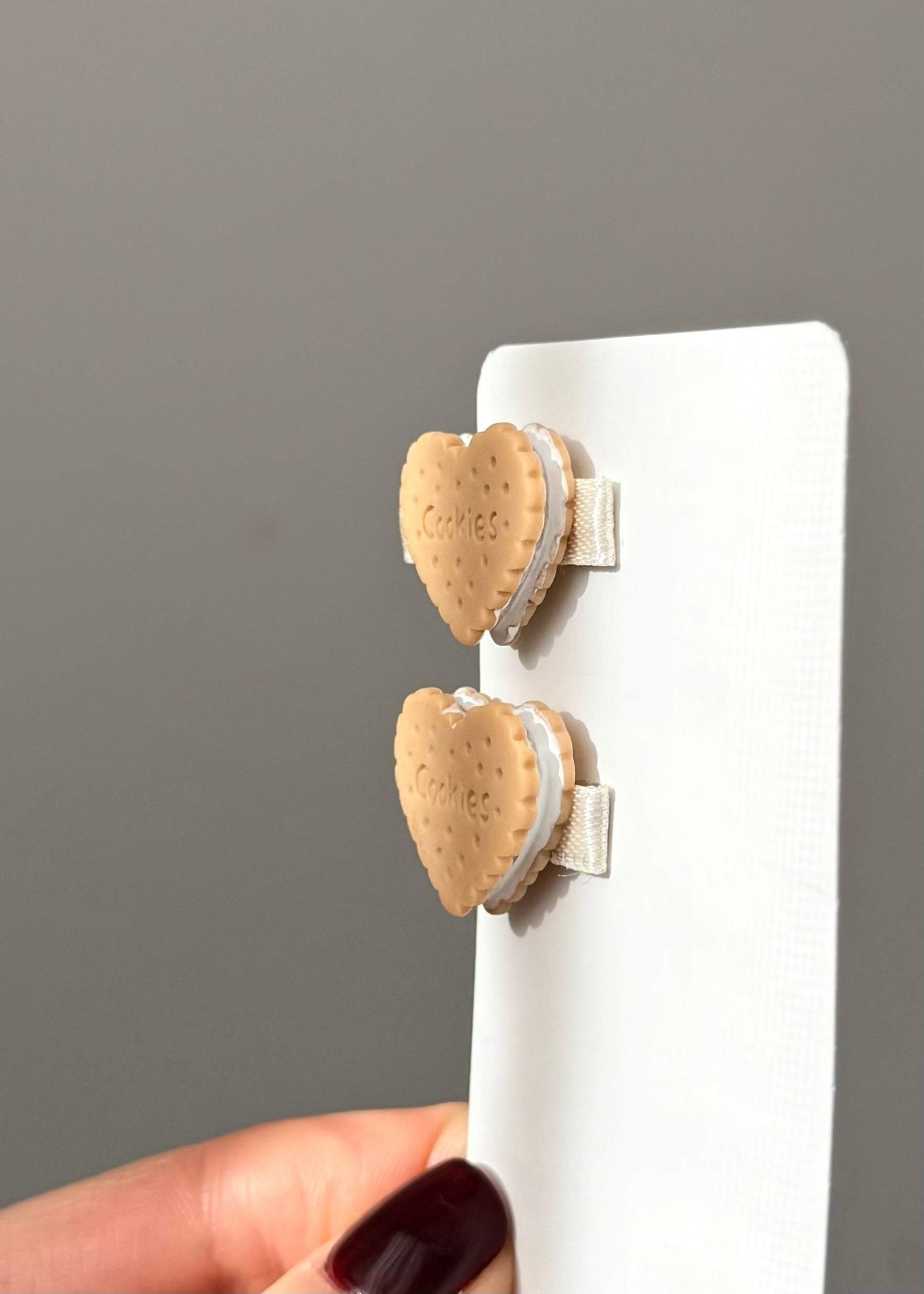 Heart-shaped cookie clips on a white board held by a hand with dark nail polish against a gray background.