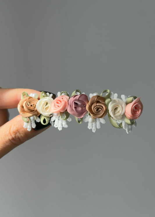 Floral barrette held by a hand against a gray background