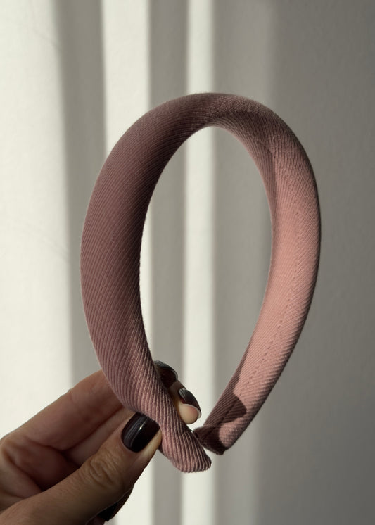 Pink hairband held by a hand against a neutral background