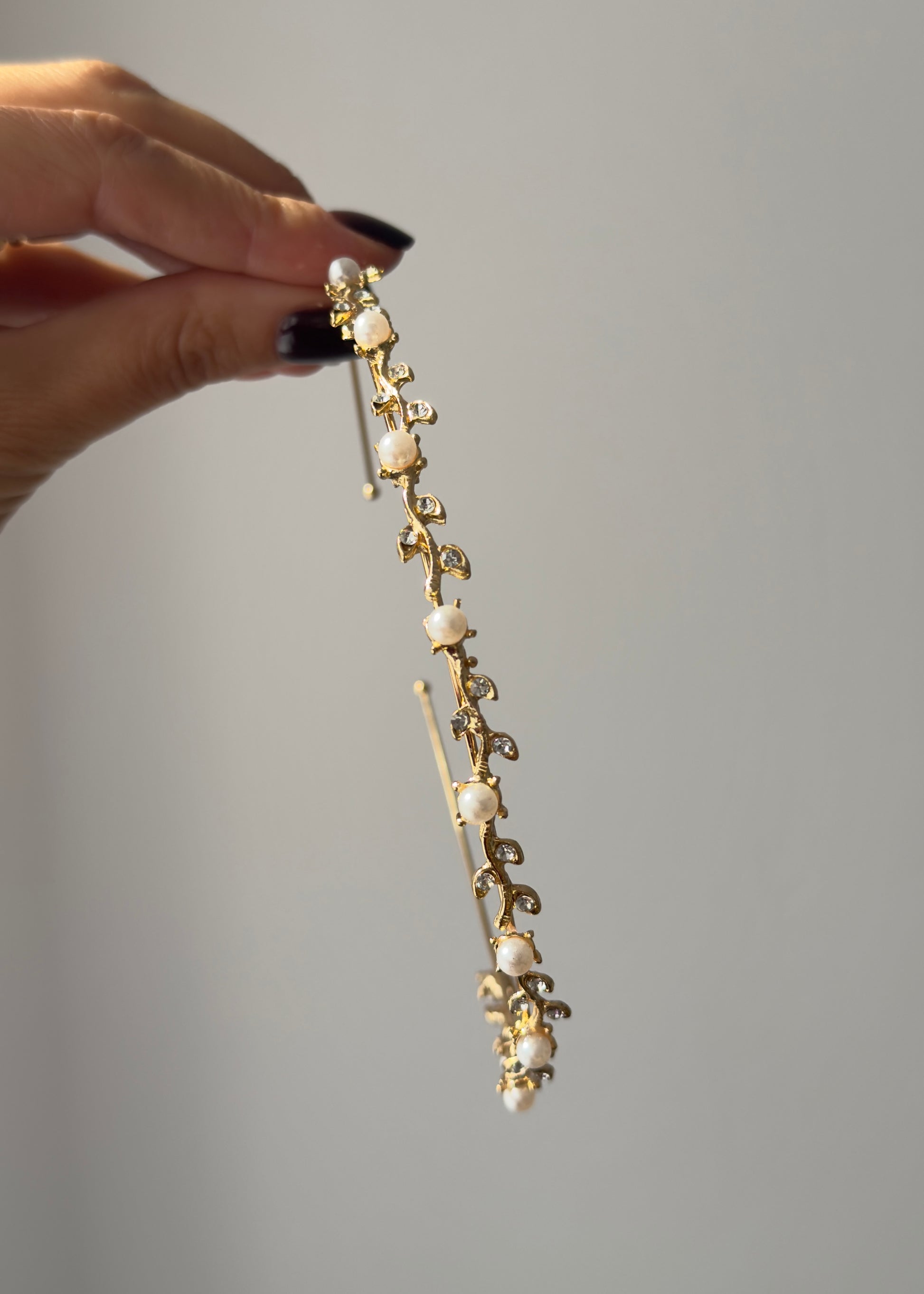 Gold hairpin with pearls held by a hand against a gray background