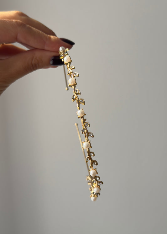 Gold hairpin with pearls held by a hand against a gray background