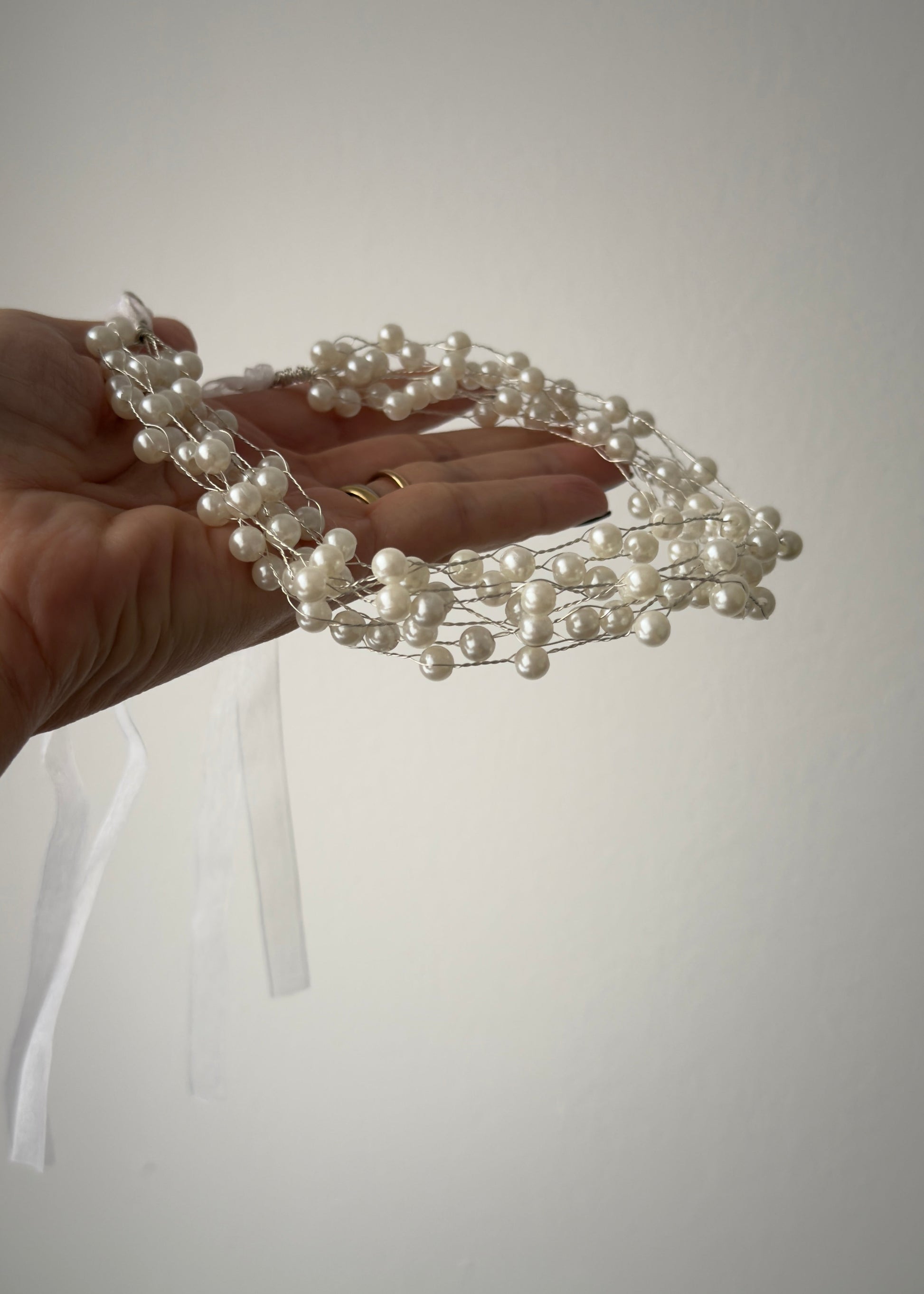 Hand holding a pearl headband against a plain background