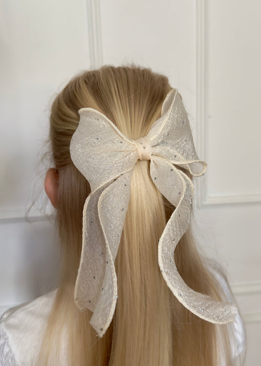 Person with long blonde hair wearing a large decorative bow in the hair against a white background