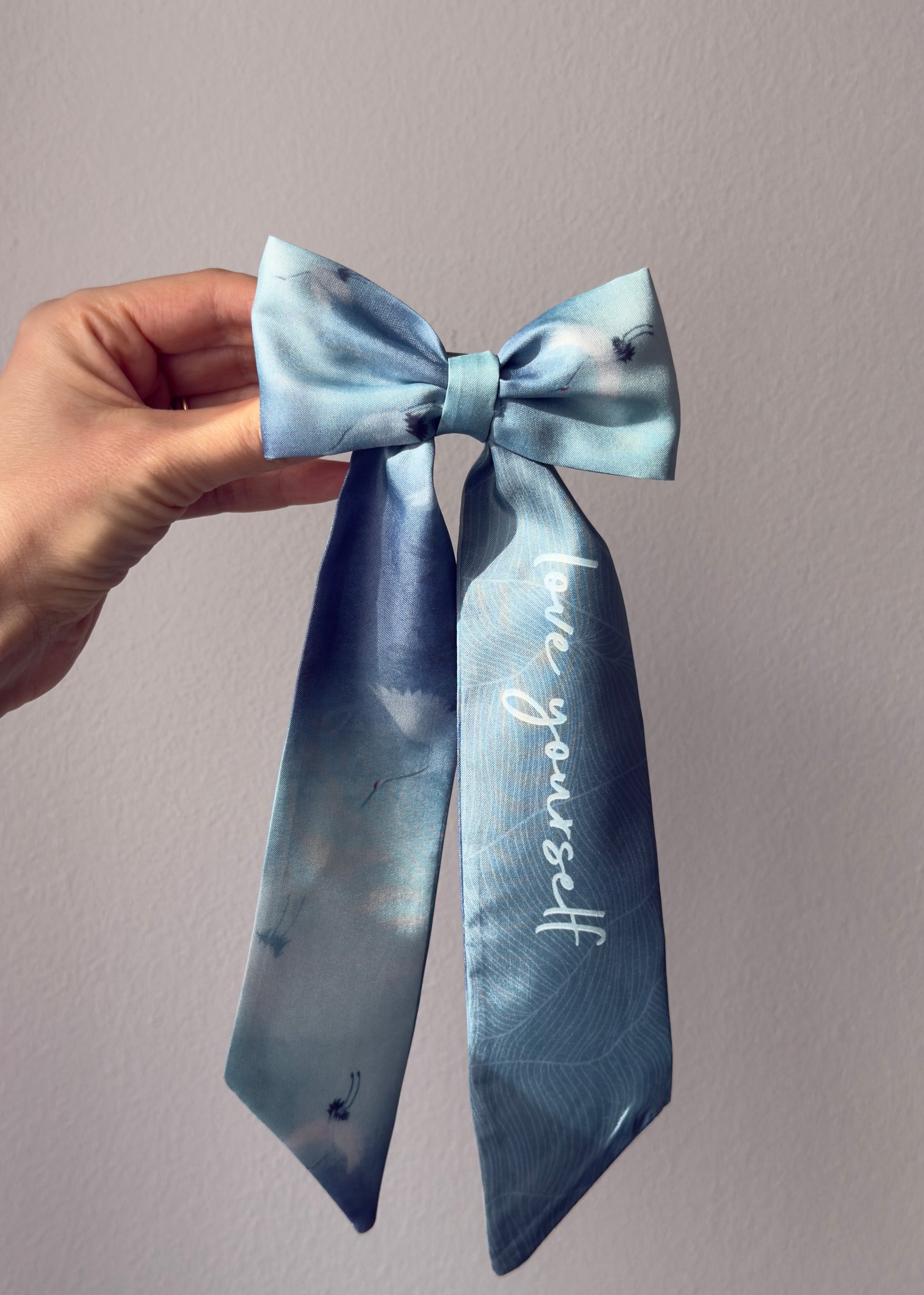 Hand holding a blue bow with 'love you more' text against a plain background